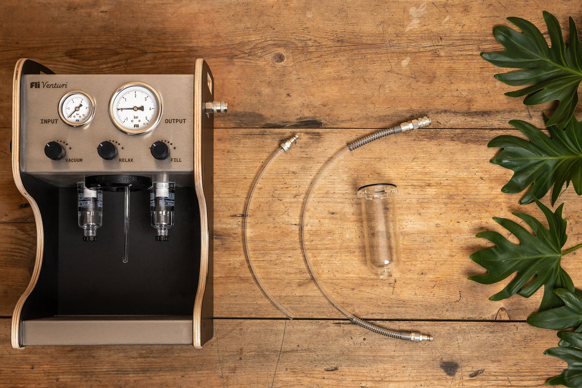 Overhead view of the FLI VENTURI Basic Set on a wooden table: vacuum pump, bleeding hose, suction hose, and clear tank arranged side by side.