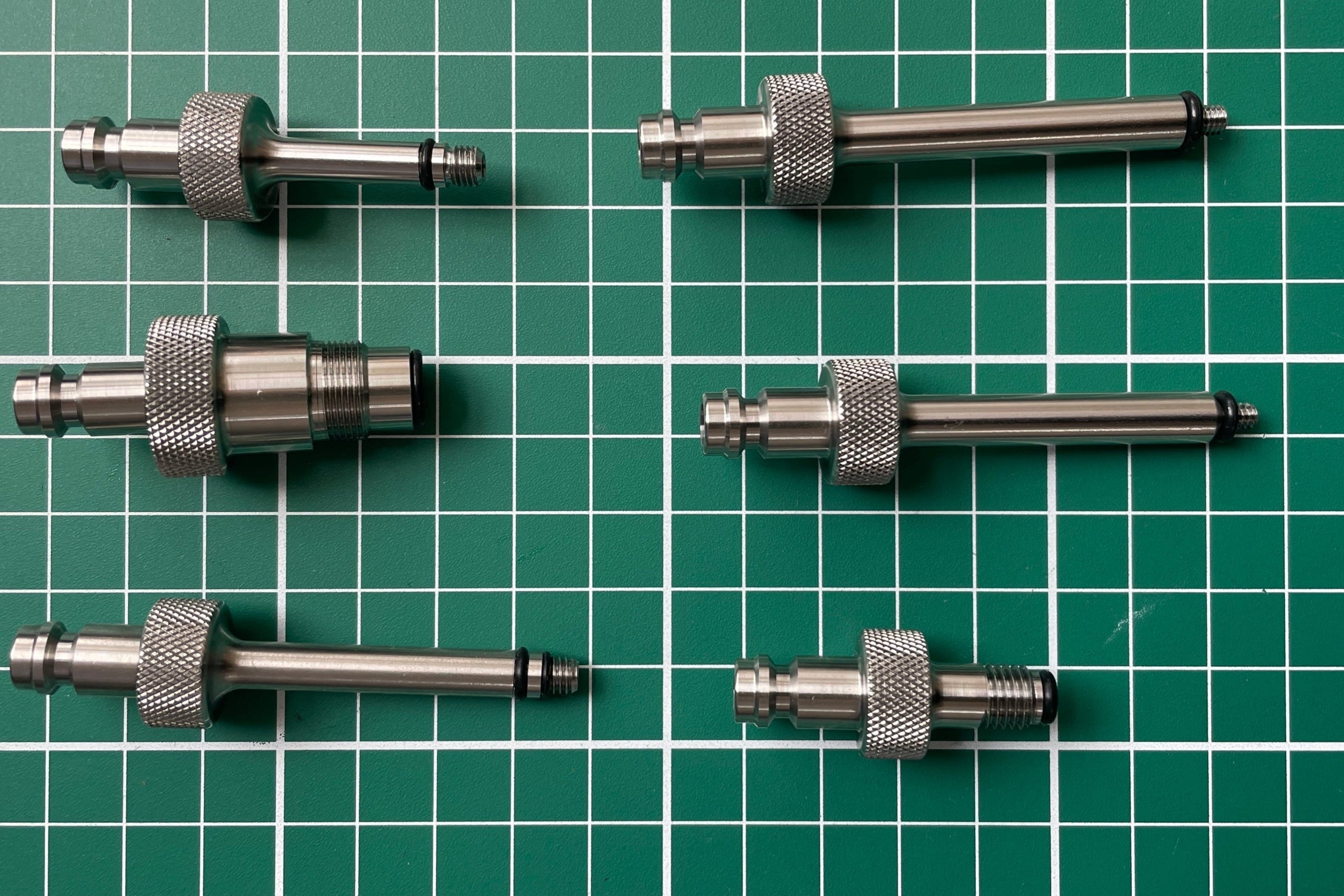 FLI Bleeding adapter: Set of six metal cylindrical components on a green grid background