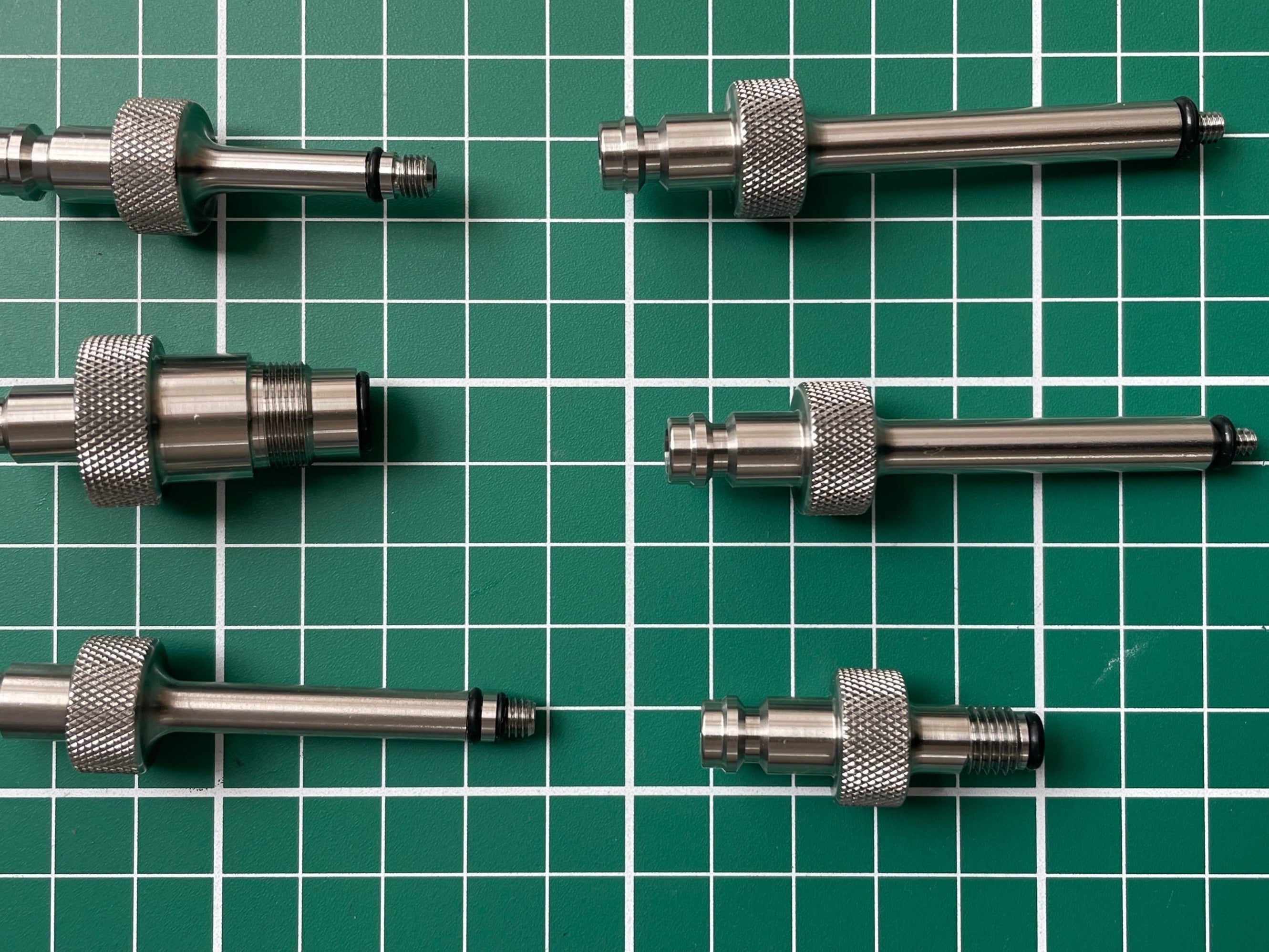 FLI Bleeding adapter: Set of six metal cylindrical components on a green grid background