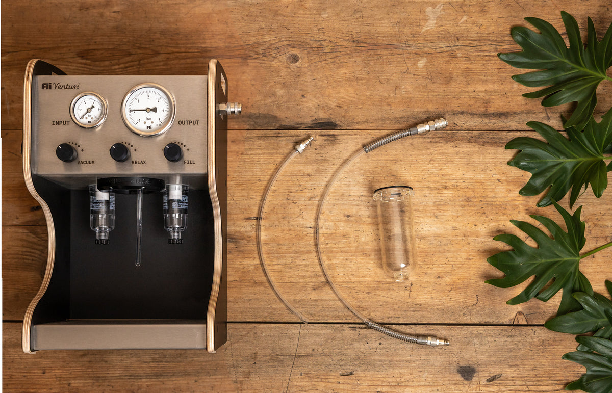 Overhead view of the FLI VENTURI Basic Set on a wooden table: vacuum pump, bleeding hose, suction hose, and clear tank arranged side by side.