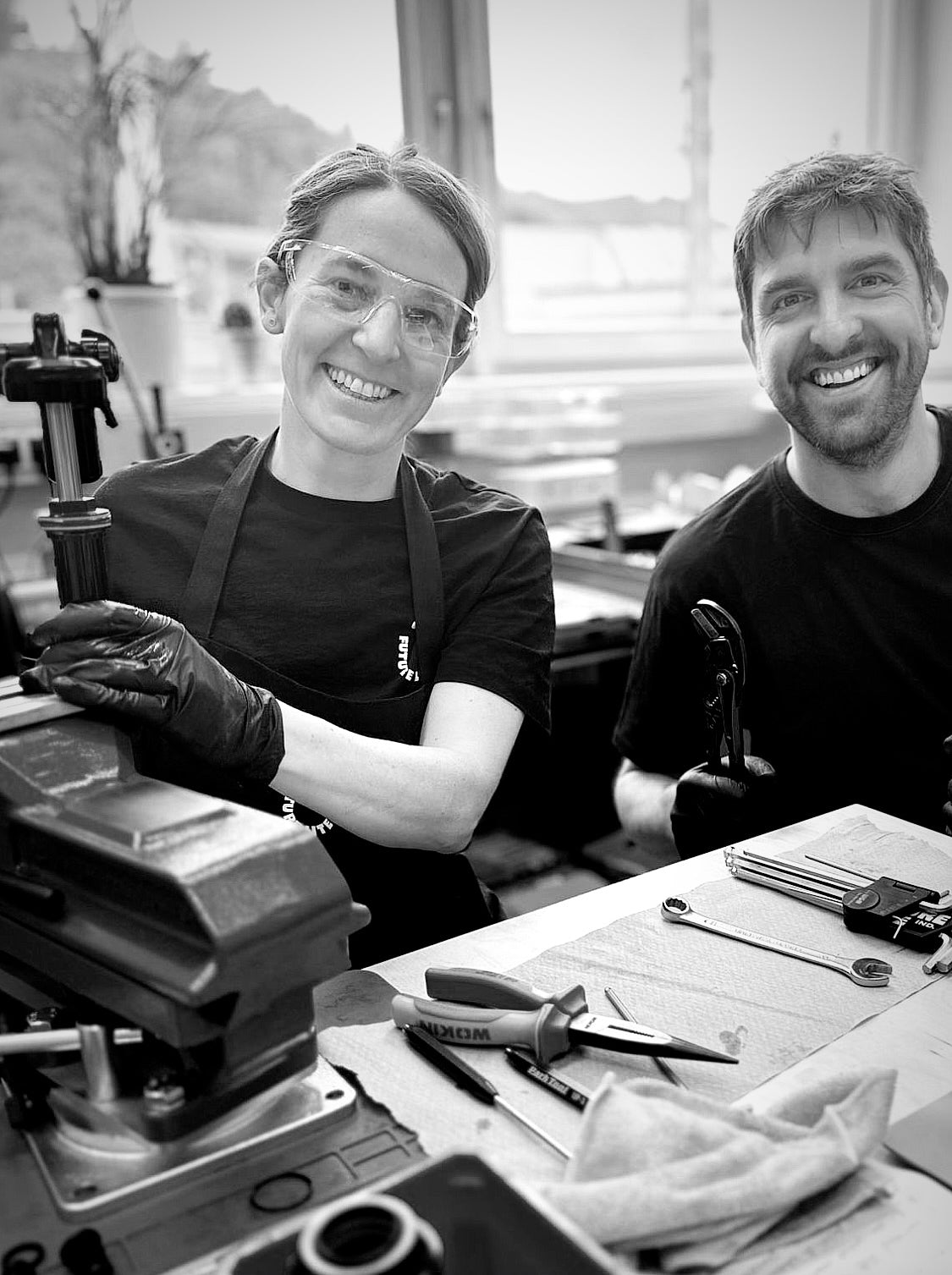 Two people in a MTB suspension workshop setting with tools and equipment.