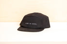 A black five-panel cap with 'KIND IS COOL' embroidered in white on the front, displayed on a white surface.