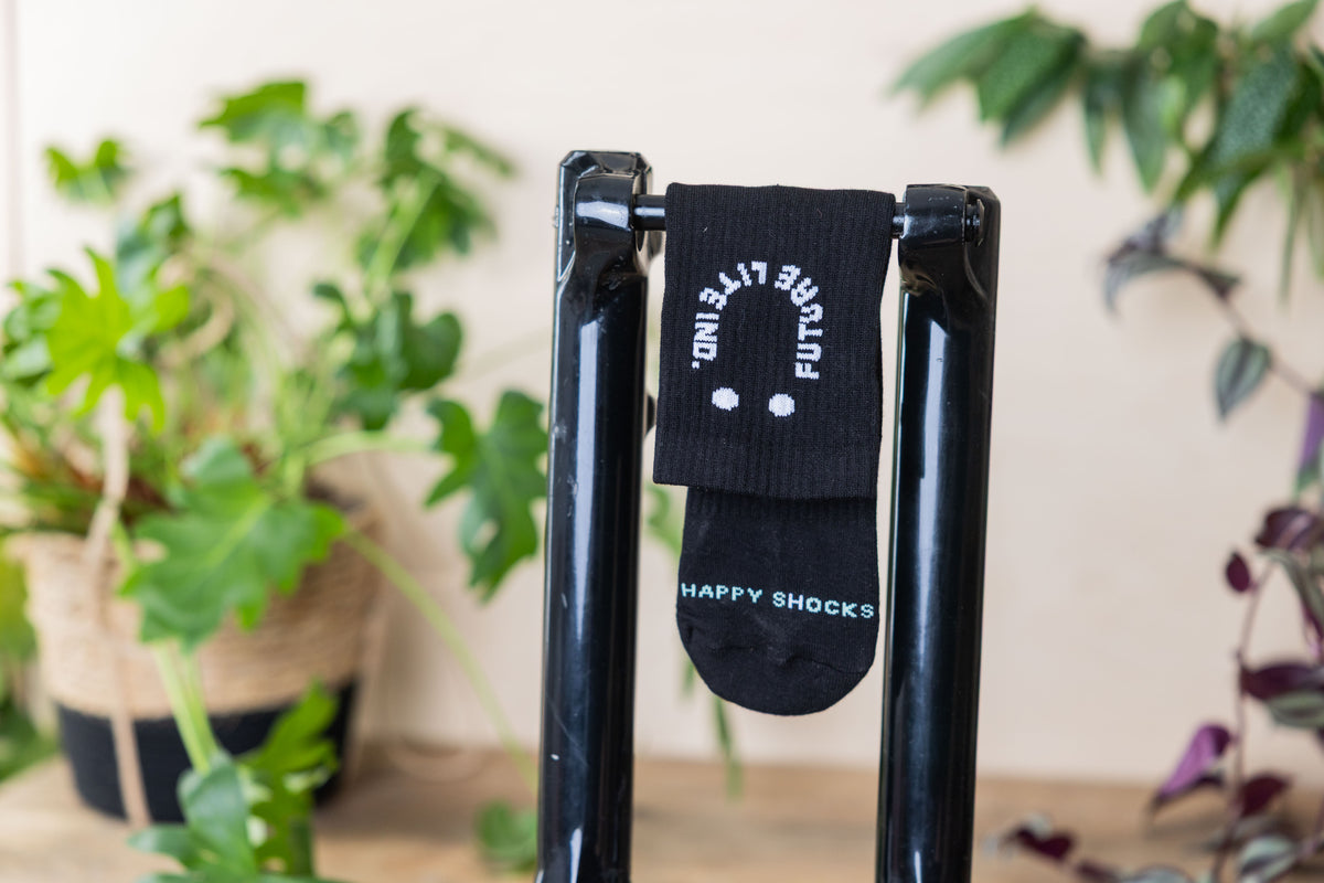 black sock with the letters happy s(h)ocks and a smiling logo hanging on a mtb suspension