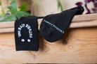 Two black socks with the letters happy s(h)ocks and a smiling logo on a wooden background