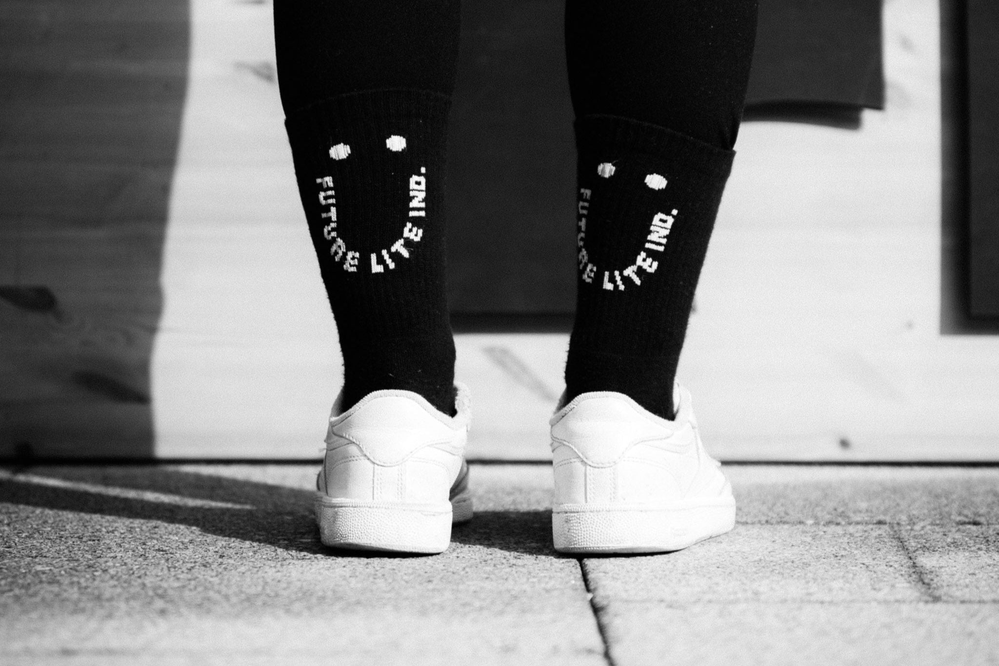 Rear view of legs wearing black MTB socks designed with a smiley face visible to the person behind.