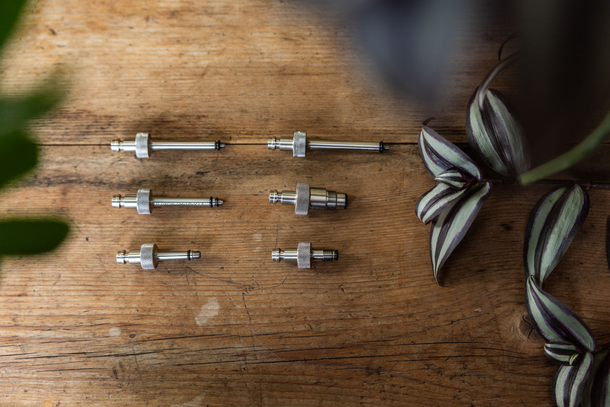 Bird's-eye view of six precision stainless steel adapters for MTB shock bleeding on a wooden table.